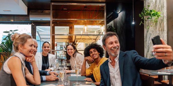 A group of six friends smiling and taking a selfie at a restaurant.