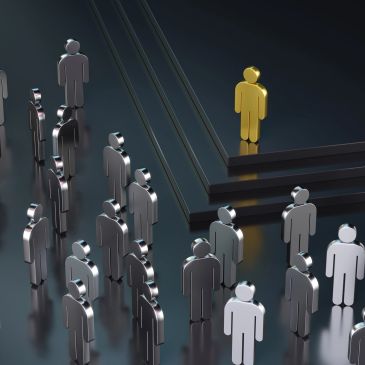 Golden figure stands apart from silver figures on black steps symbolizing leadership or uniqueness.