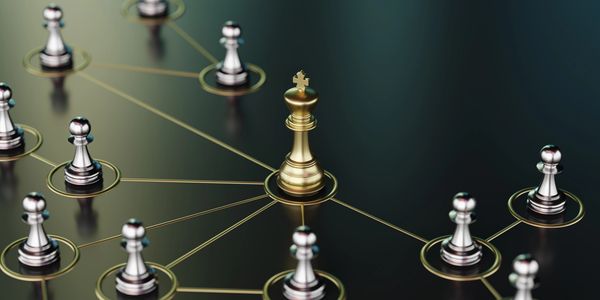 Golden king chess piece connected to silver pawns on a dark surface.