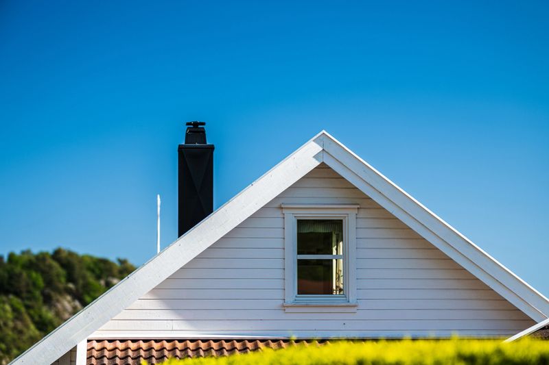 White gable roof house with chimney under blue sky.