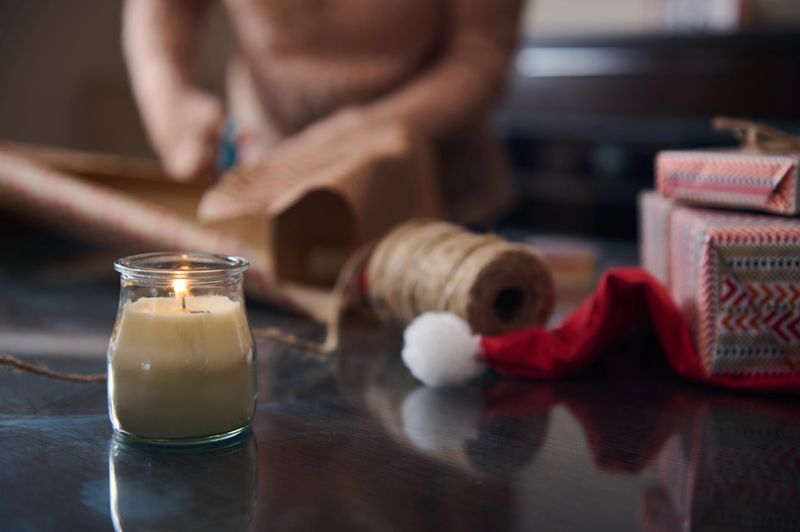 Warm and cozy scene of gift wrapping during the holiday season, featuring festive decorations, a glowing candle, and a Santa hat. The image captures the joy and creativity of Christmas preparations.