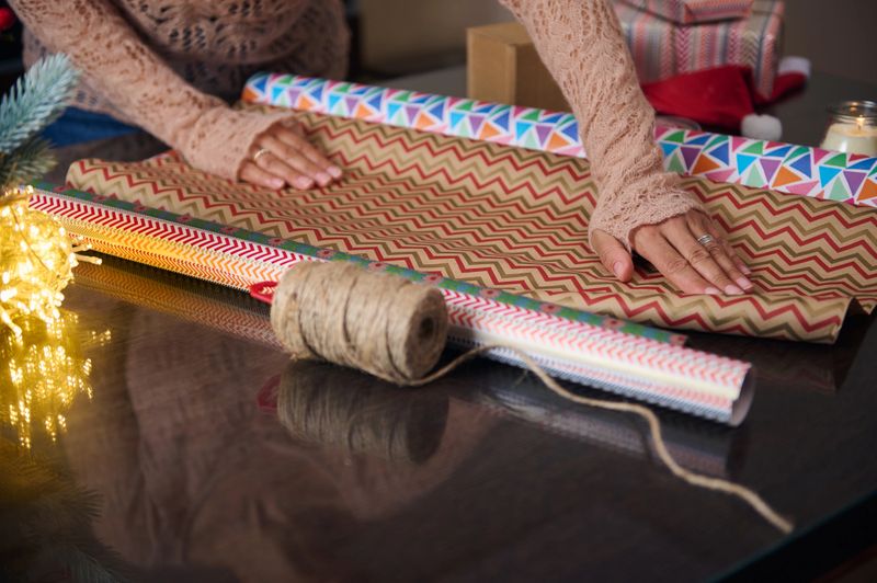 A close-up of hands wrapping gifts with colored paper, surrounded by decorations. This festive scene captures the spirit of holiday preparations, showcasing creativity and care while wrapping presents.