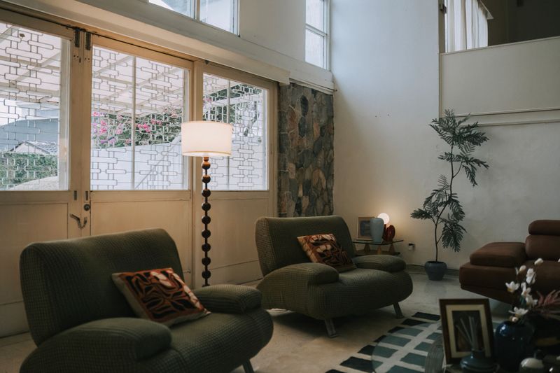 stylish mid-century modern living room with textured armchairs, a floor lamp, stone accent wall, indoor plant, and soft ambient light—ideal for themes of interior design, homestay, and cozy lifestyle.
