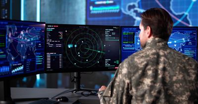 Military personnel monitoring aircraft and global data on multiple high-tech screens.