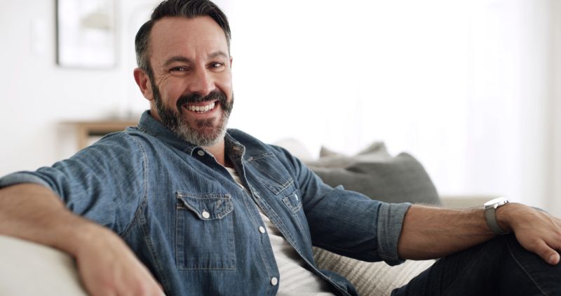 Portrait, man and relax with smile at house for peace, start day and comfortable of weekend break. Happy, mature male person and chilling on couch for free time, cozy homeowner and unwind of wellness
