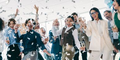 A group of diverse professionals celebrating joyfully with confetti and drinks.