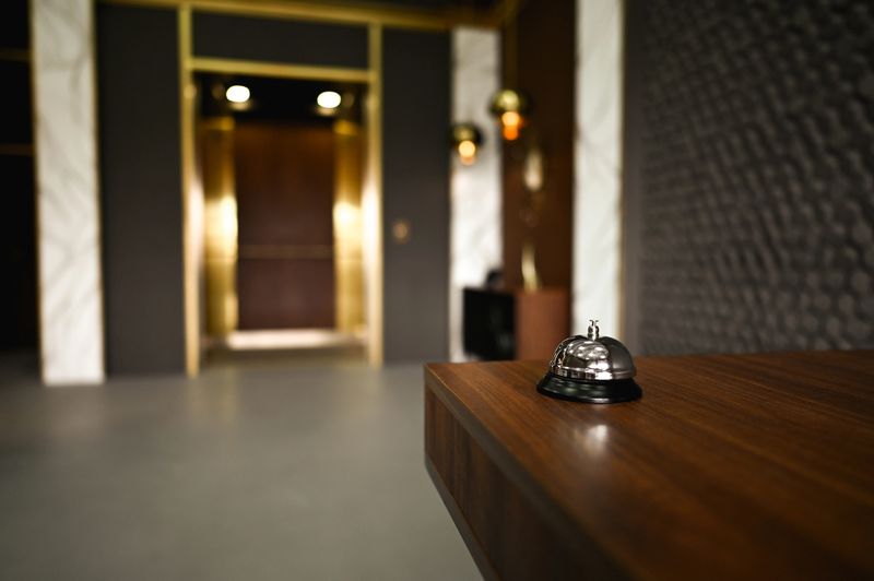 Shiny service bell on wooden desk with elevator in background in elegant hotel lobby