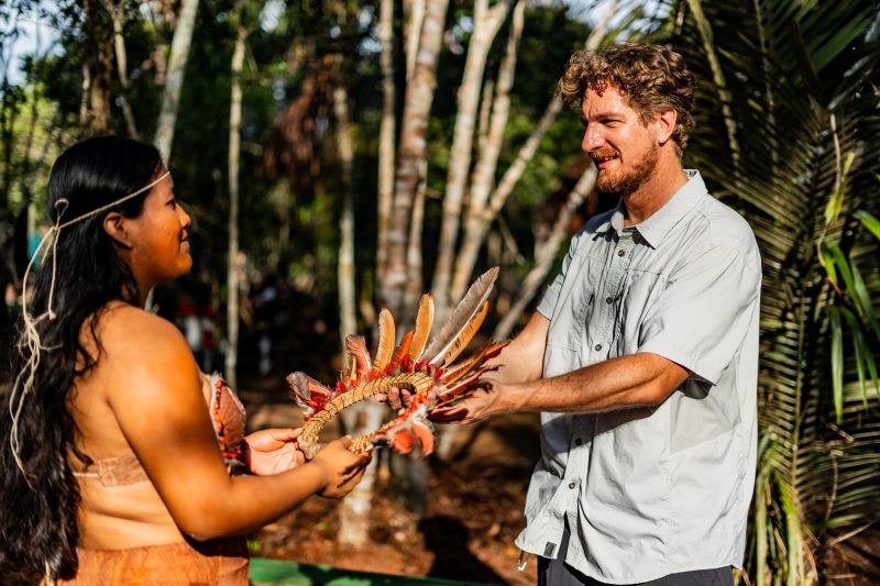 Tourist receiving a traditional Curripaco headdress from an indigenous woman during a village visit
