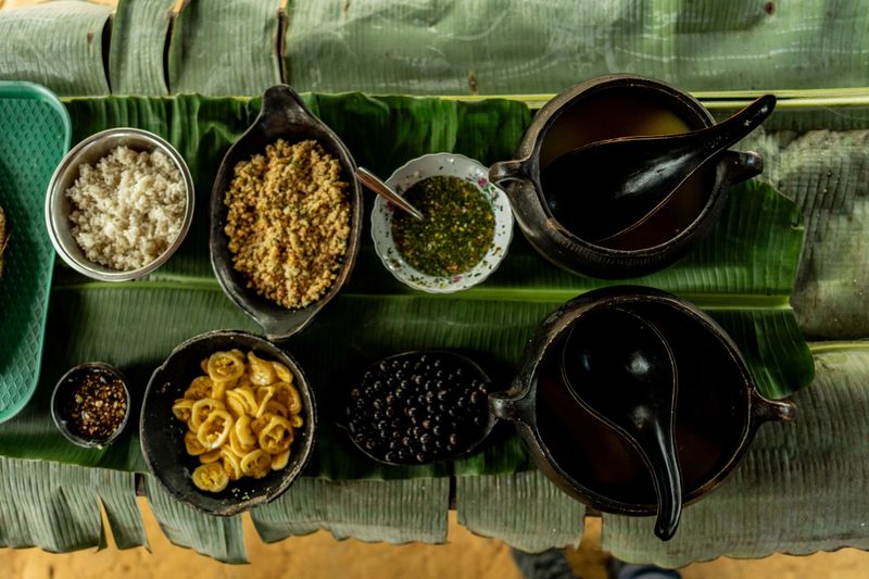 Traditional gastronomic presentation displays ancestral culinary diversity with multiple foods served in ceramic utensils and banana leaves, representing Curripaco community food richness and preservation of millenary Amazonian culinary techniques in authentic cultural context