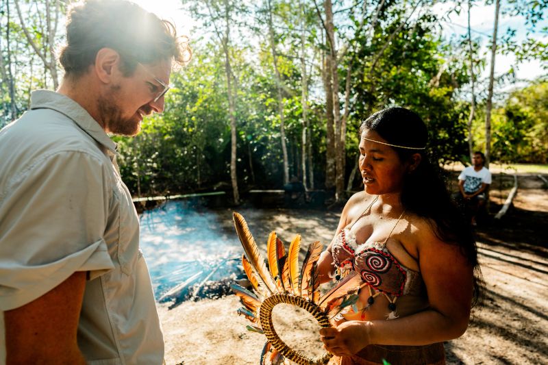 Tourist receiving a traditional Curripaco 'ancestral feather crown' from an indigenous woman during a village visit