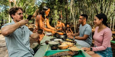 People sharing a meal outdoors with indigenous hosts.