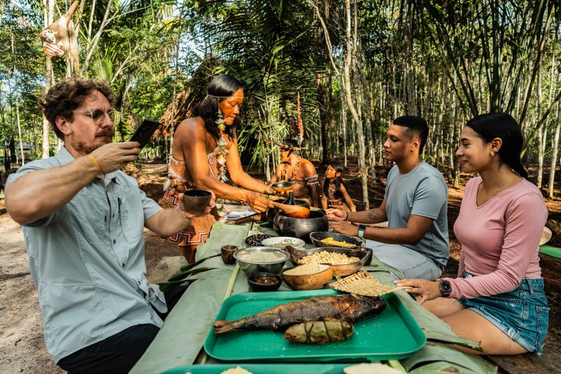 Curripaco community member demonstrates traditional hospitality offering ancestral cuisine to visitors in natural village environment, promoting respectful gastronomic exchange and appreciation of millenary culinary techniques through sustainable Amazonian ethnic tourism experience that connects cultures