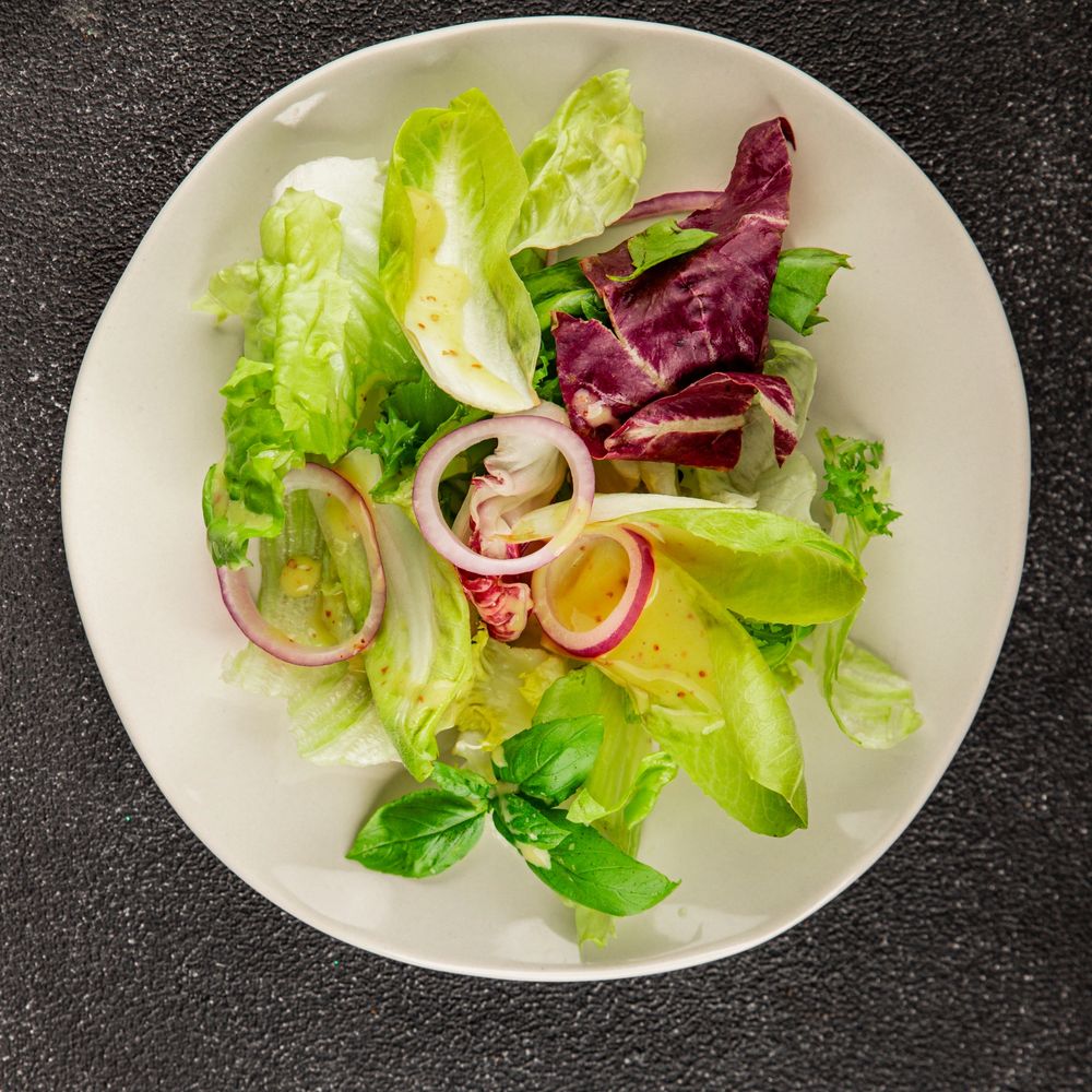 Fresh mixed salad with lettuce, red onion, and basil on a white plate.