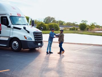 Two men shaking hands near a truck in a parking lot.