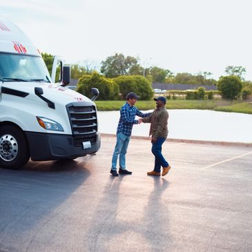 Two men shaking hands near a white semi-truck in a parking lot.