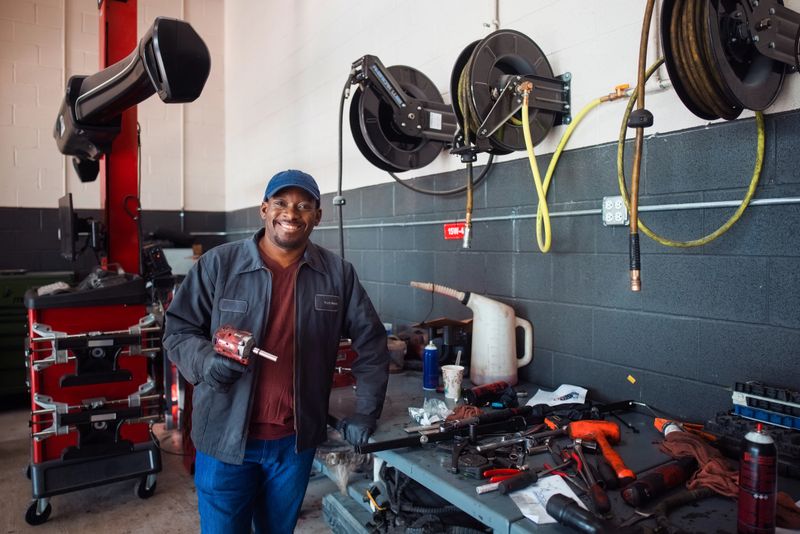 Automotive technician smiling while working in a professional repair shop, surrounded by tools and equipment, demonstrating expertise in car maintenance, tools' organization, and dedication to the engineer profession.