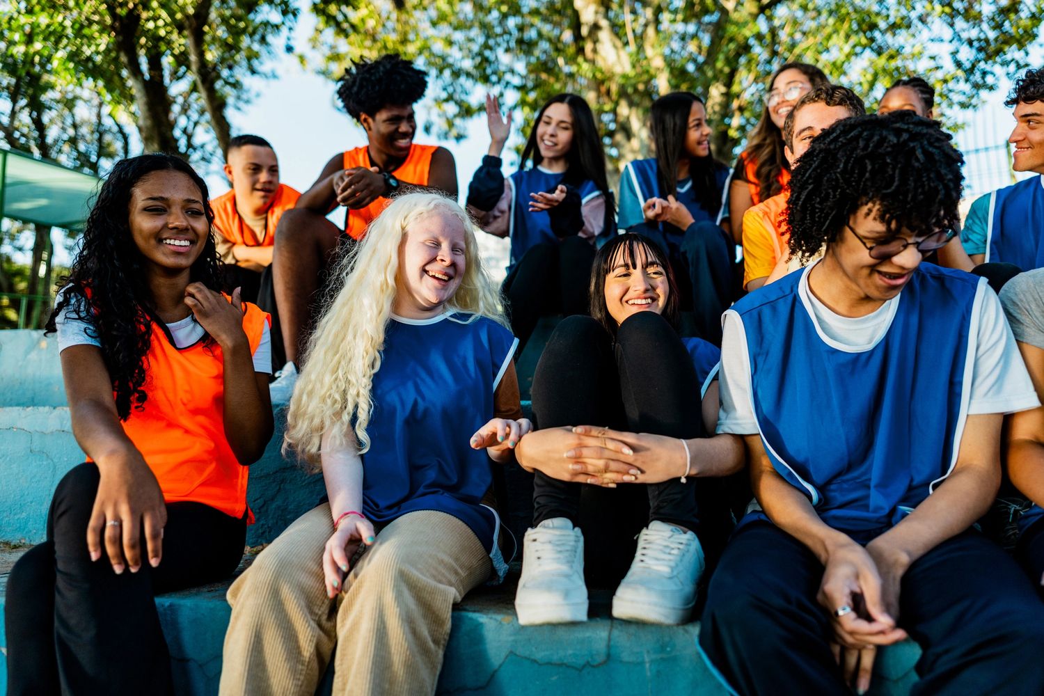 A diverse group of young people in sports vests smiling and enjoying time outdoors.