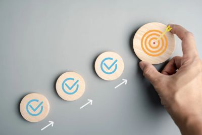 Hand placing a target piece after checkmark progress icons on a gray background.