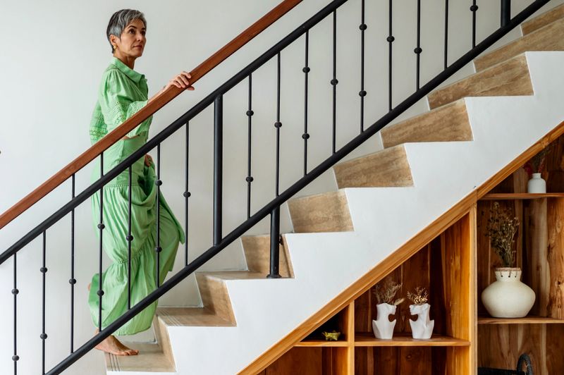 Woman in green attire ascending an elegant staircase, surrounded by wooden furnishings and modern decor, conveying a sense of everyday living in a stylish and comfortable environment.