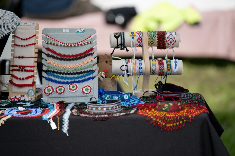 A colorful collection of handmade beaded necklaces and bracelets displayed on a black tablecloth at an outdoor market. The intricate designs and vibrant patterns showcase traditional craftsmanship and cultural artistry.