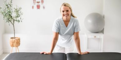 Smiling woman leaning on a massage table in a bright room.