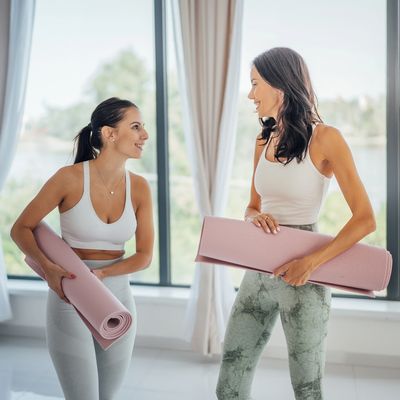 Two women holding yoga mats and smiling indoors.