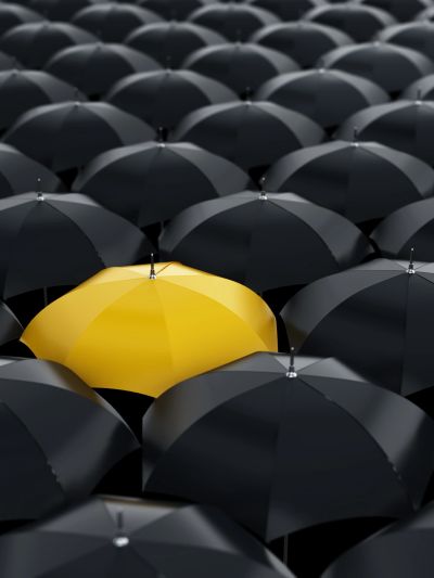 A yellow umbrella standing out among black umbrellas.