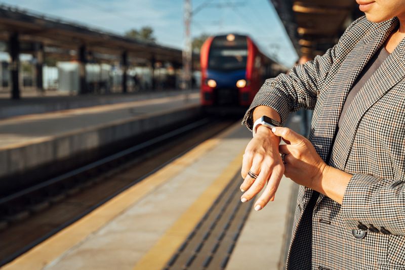 Female commuter checking smartwatch while waiting for train on railroad platform