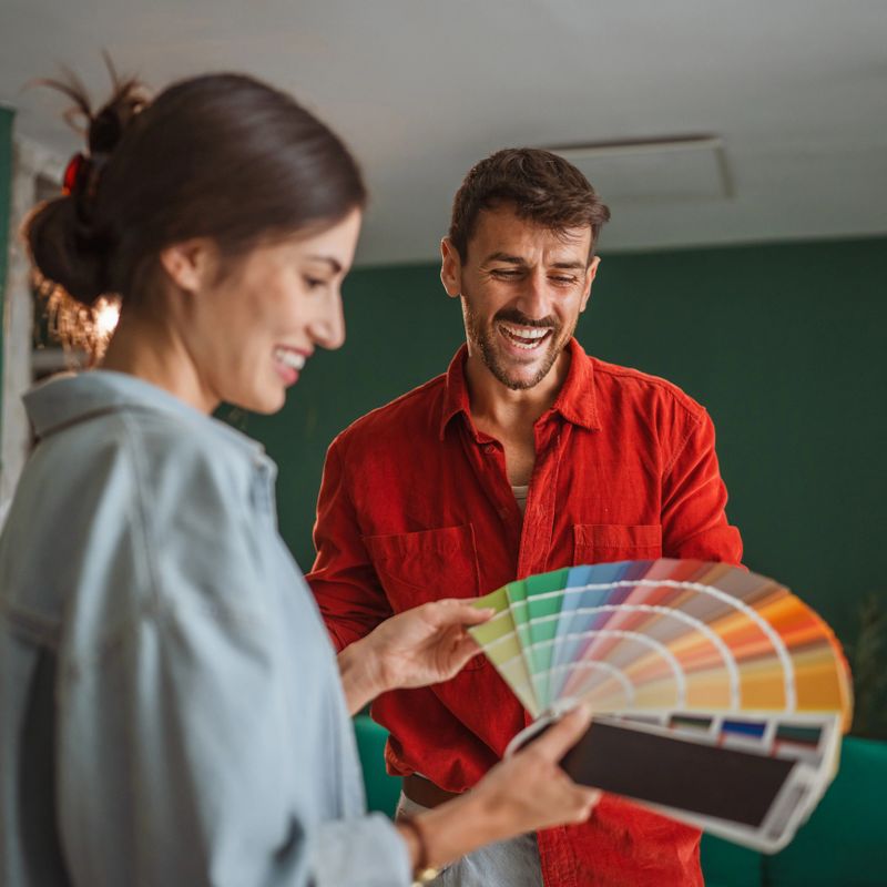 Smiling couple compares paint swatches and discusses interior design plans for their home renovation, collaborating on color choices for a modern living space