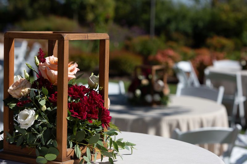 Wooden box centerpiece overflowing with fresh flowers decorating table at an outdoor wedding reception venue