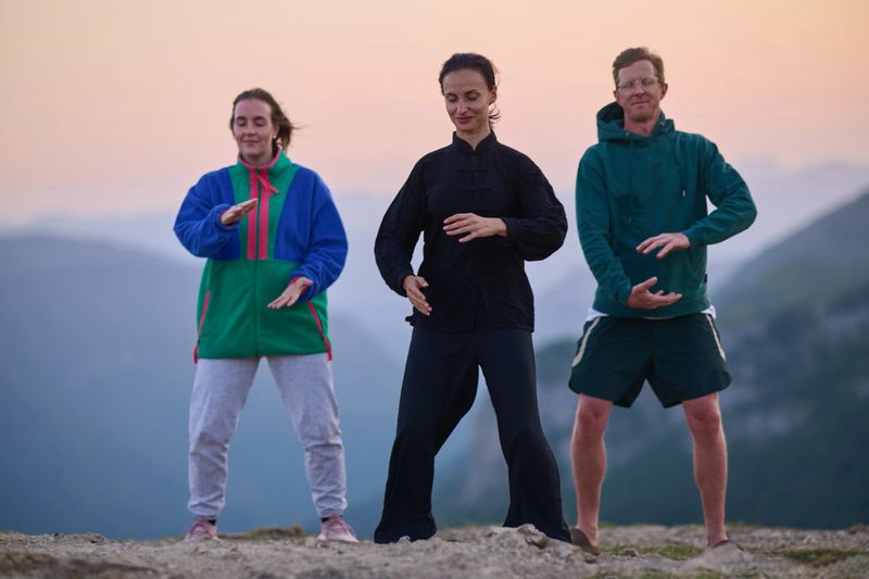 Group of people practicing Tai Chi outdoors at sunrise on mountain, performing slow meditative movements for balance, energy, health, and mindfulness in nature