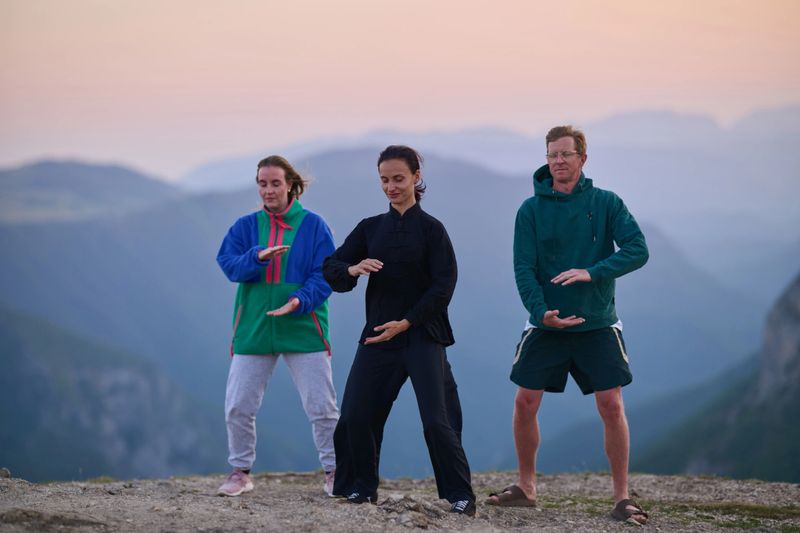 Group of people practicing Tai Chi outdoors at sunrise on mountain, performing slow meditative movements for balance, energy, health, and mindfulness in nature