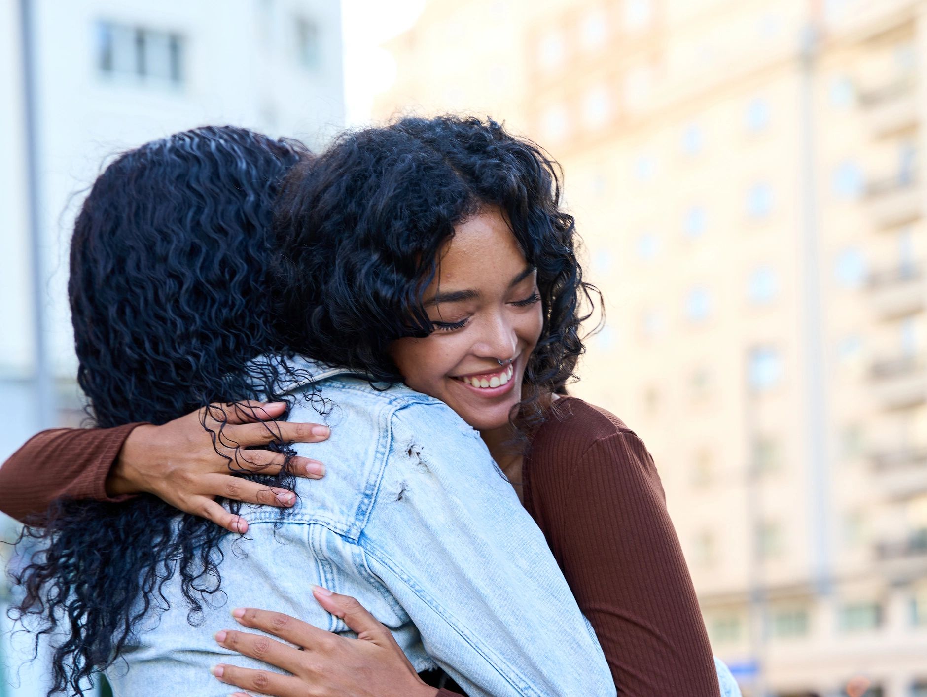 Two women warmly hugging each other outdoors with smiles.