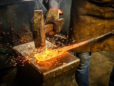 Blacksmith hammering glowing hot metal on an anvil, sparks flying.