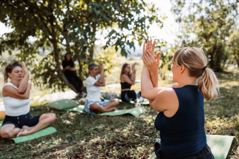 Group of women sitting in lotus pose on mats outdoors, eyes closed, guided by an instructor during a peaceful yoga and meditation retreat focused on wellness and mindfulness