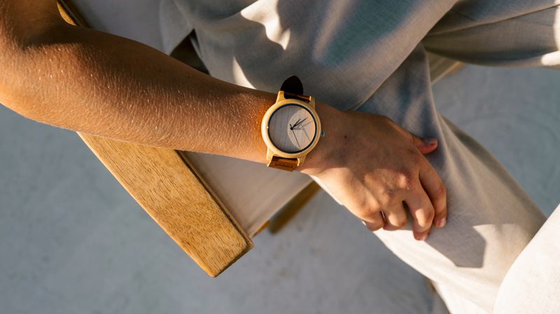 Close-up of a wooden wristwatch with a leather strap on a person's wrist. The light creates a warm and inviting feel.