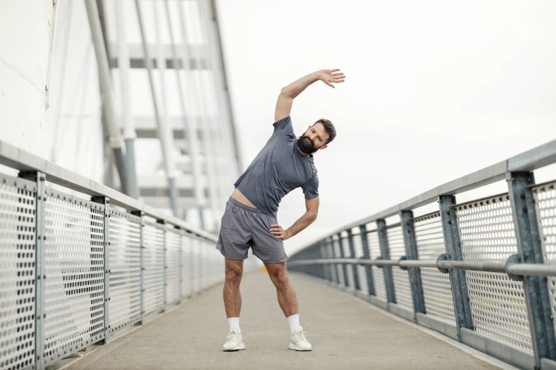 Fit muscular athlete standing on a bridge and doing warmup exercises on a bridge.