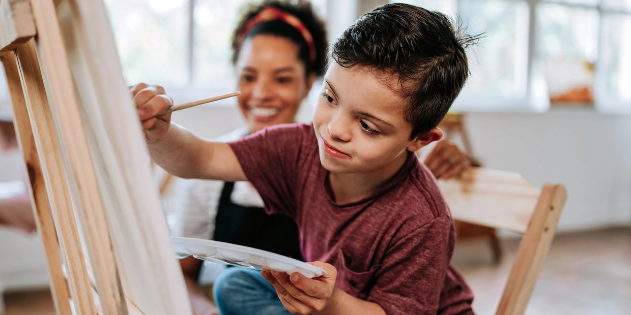 Children painting on easels while a teacher smiles supportively.