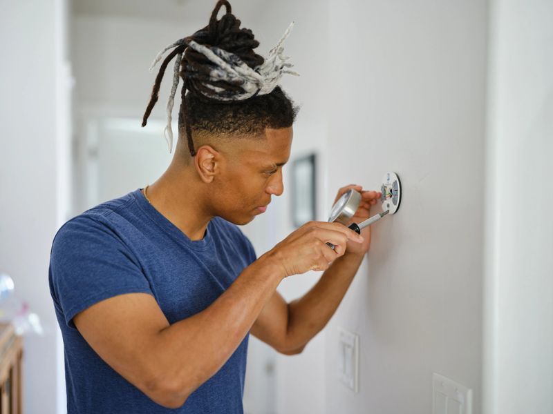 A young man in a home installing a smart thermostat.