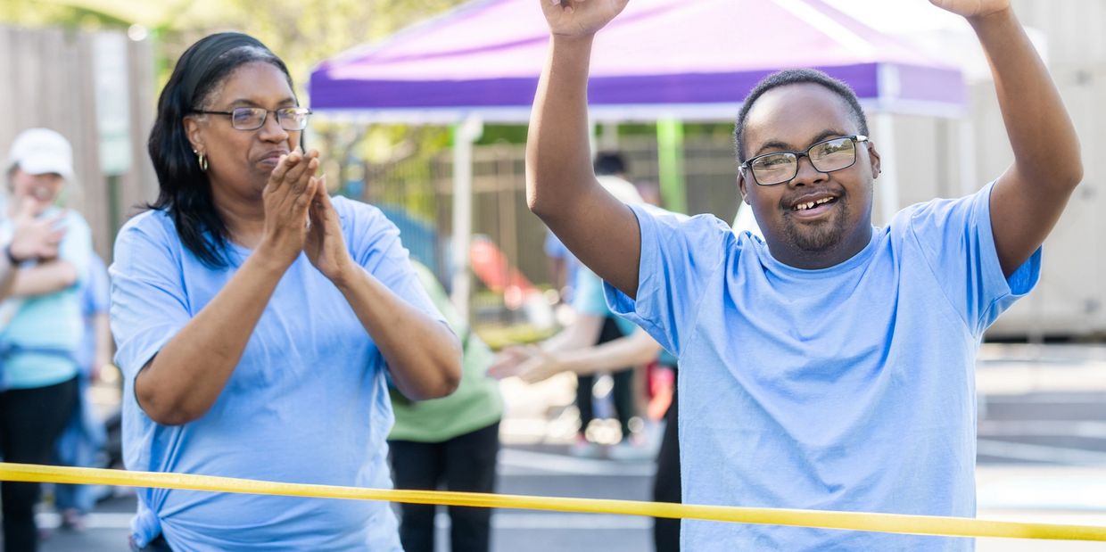 A man with Down syndrome crosses a finish line, celebrating with a woman clapping.