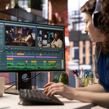 A woman edits a podcast video on a dual monitor setup in a cozy workspace.