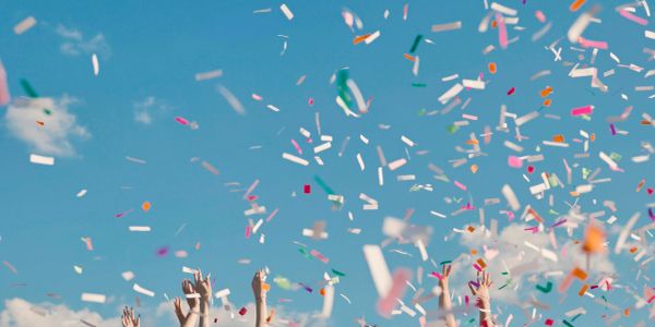 Hands raised in celebration with colorful confetti in the sky.