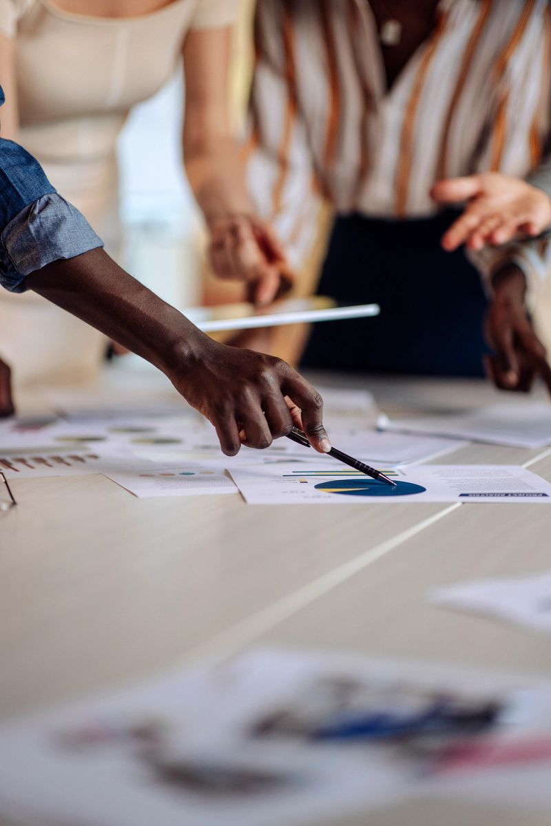 A group of professionals collaboratively discussing data displayed on papers and a tablet, emphasizing teamwork, strategy, and cooperation during a business meeting or project analysis