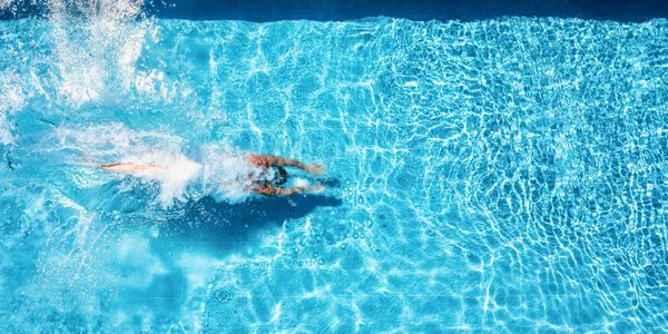 Person swimming underwater in a bright blue pool.