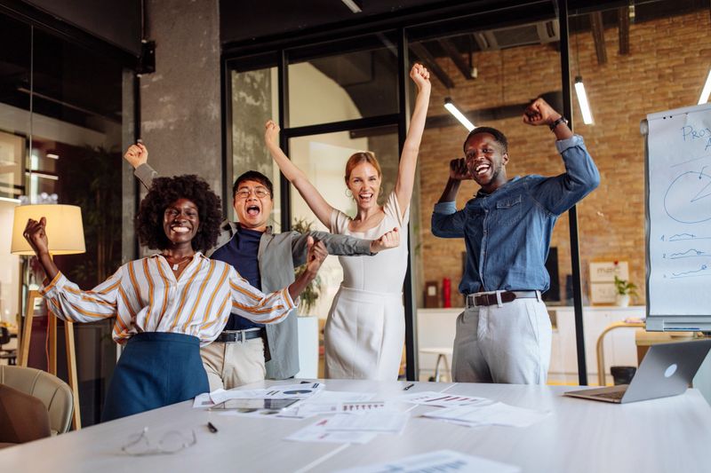 Team of diverse professionals celebrating success in a modern office setting, conveying joy, achievement, motivation, and teamwork through their dynamic and enthusiastic expressions