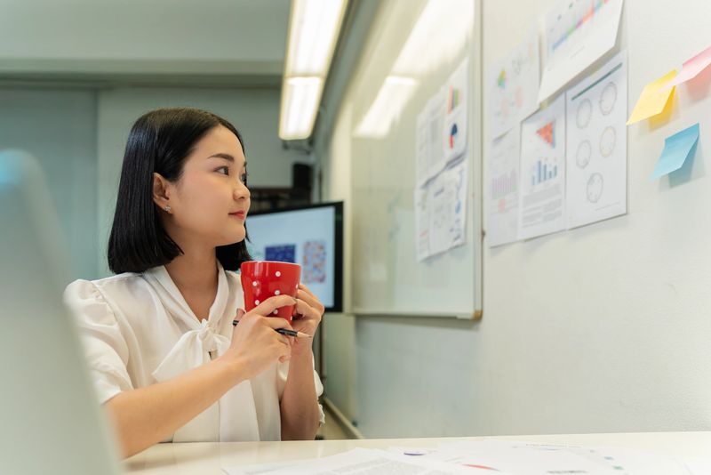 An Asian female researcher arranges genomic and scientific charts on a wall in a laboratory workspace. The scene emphasizes data analysis, visualization, and authentic scientific workflow in biomedical research.