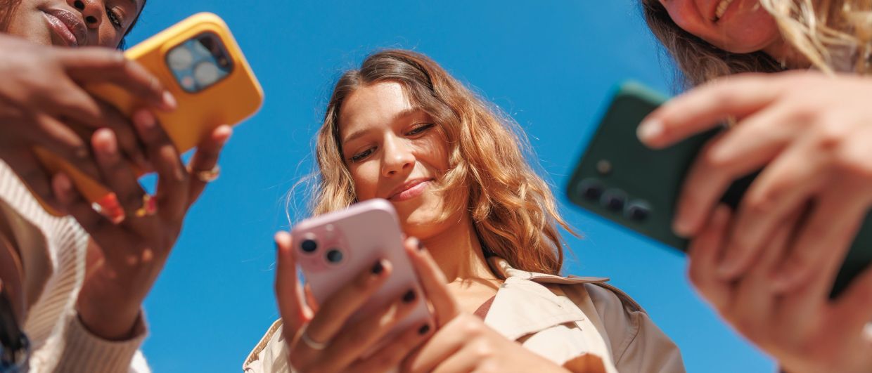 Three people smiling while looking at their phones.