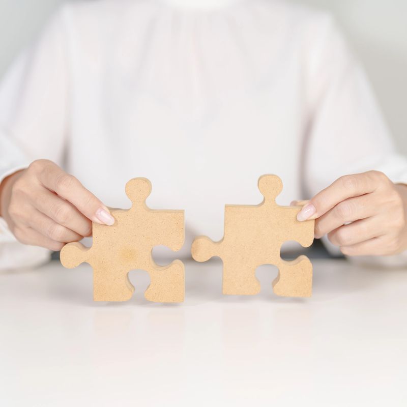 Woman connecting couple puzzle piece, wood jigsaw on table. Business solutions, mission, success, goals, strategy, Teamwork, Idea, Solution and challenge concepts