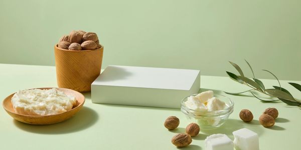 Natural shea butter with nuts and leaves on a light green background.