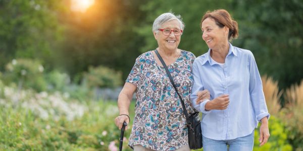 Two elderly women walking outdoors arm in arm.